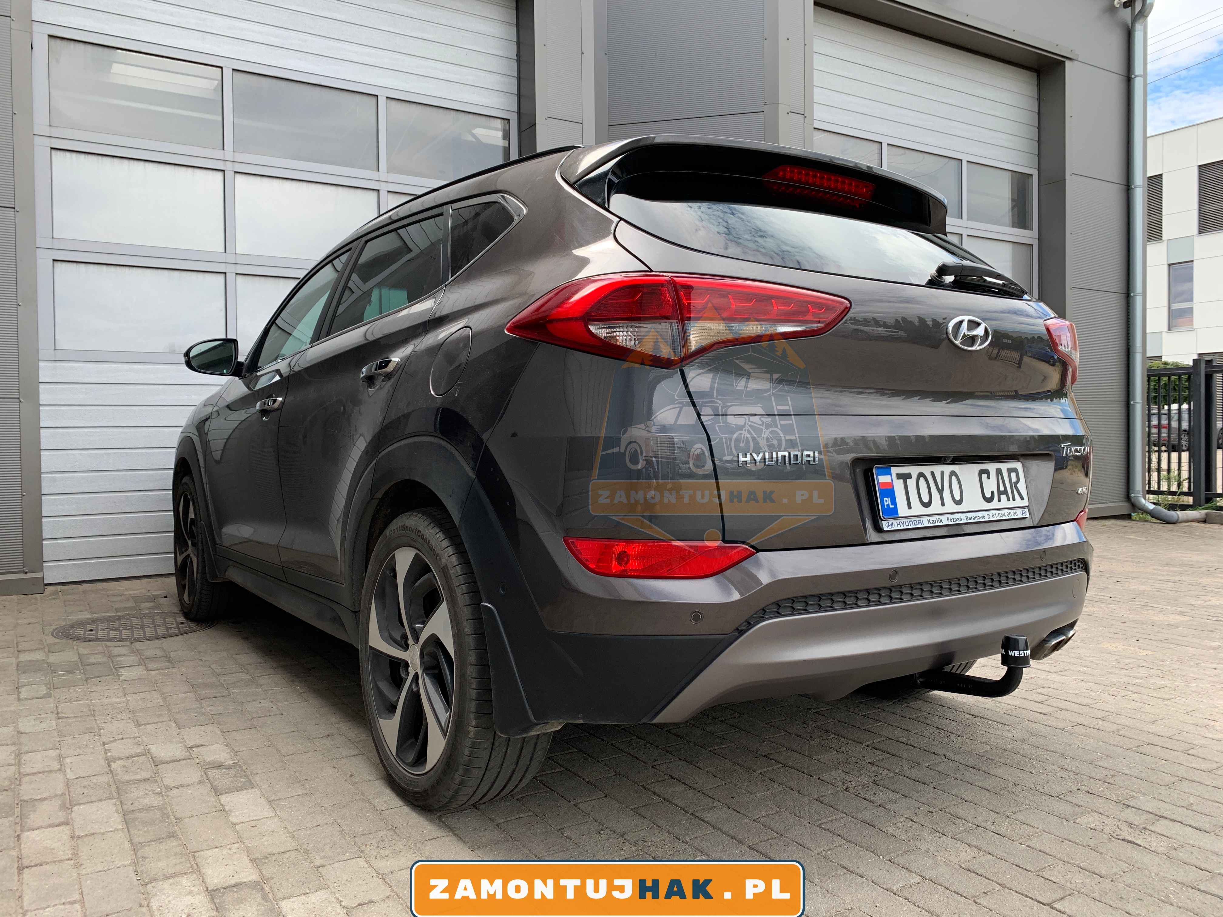 Zdjęcie Hyundaia Tucsona z zamontowanym hakiem holowniczym westfalia A40V, zdjęcie zostało zrobione z tyłu, z lewej strony samochodu na tle serwisu zamontujhak.pl